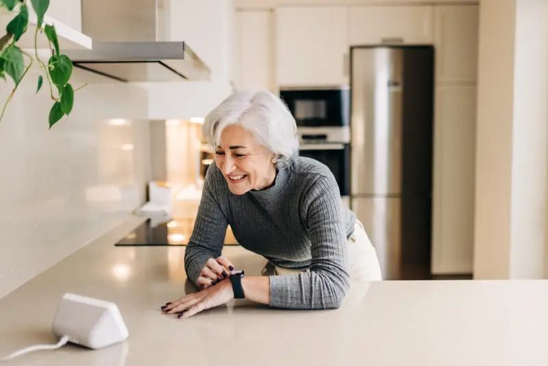 Senior woman speaking to her smart home device in her kitchen.